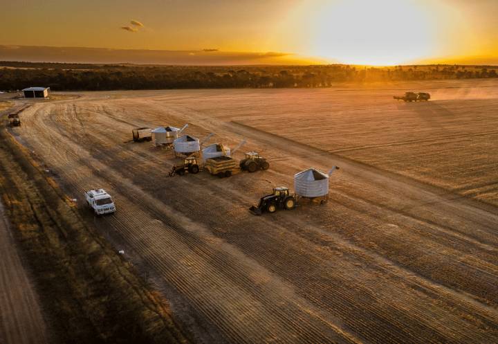 Aerial view of paddock at sunset with farm vehicles working in the field