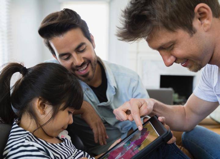 Male couple looking at tablet with their daughter.