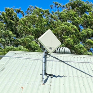 A diamond-shaped antenna, known as an nbn Wireless Network Terminating Device Version 2, on house roof with trees in the background